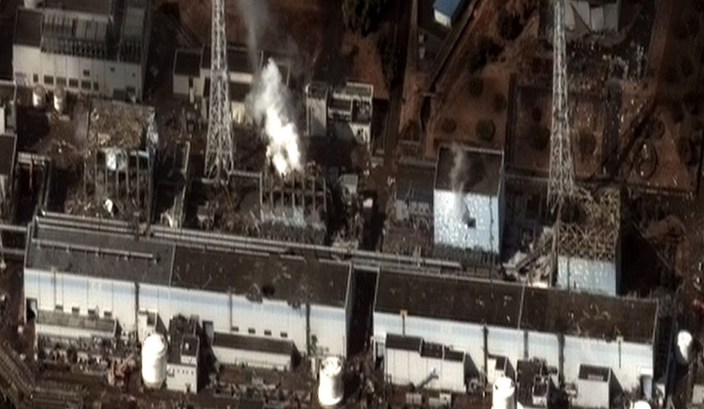 The four damaged reactor buildings (from left: Units 4, 3, 2, and 1) on 16 March 2011. Hydrogen-air explosions in Unit 1, 3, and 4 caused structural damage.