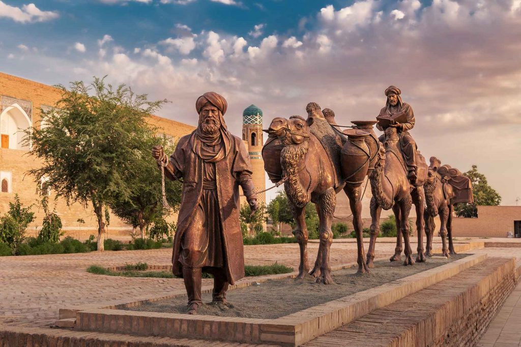 A sculpture of a camel carrying goods and a man in Uzbek dress front of the city walls at Khiva Uzbekistan